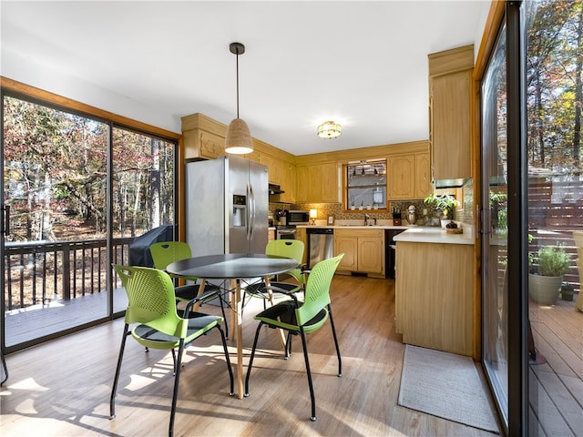 kitchen featuring appliances with stainless steel finishes, tasteful backsplash, sink, light hardwood / wood-style flooring, and hanging light fixtures