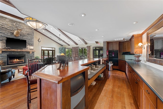 kitchen with a kitchen bar, a fireplace, light hardwood / wood-style flooring, and lofted ceiling with beams