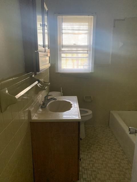 bathroom with vanity, toilet, tile walls, and a washtub