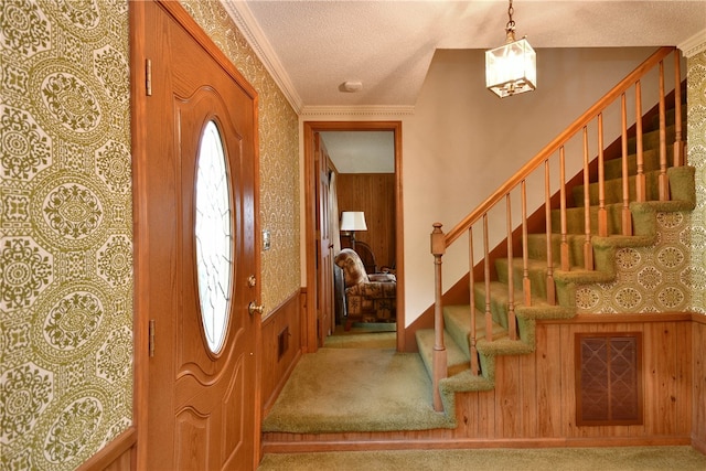 foyer entrance featuring a textured ceiling, carpet floors, crown molding, and wood walls