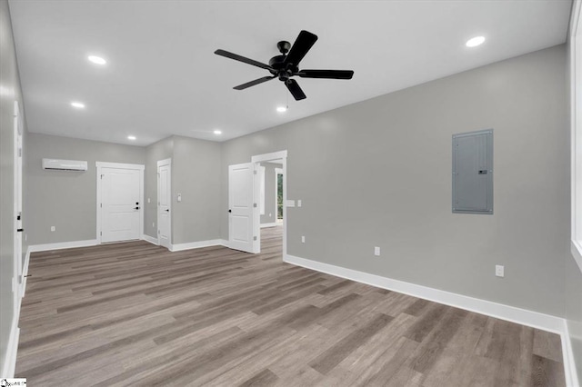 spare room featuring electric panel, ceiling fan, light hardwood / wood-style flooring, and a wall mounted air conditioner