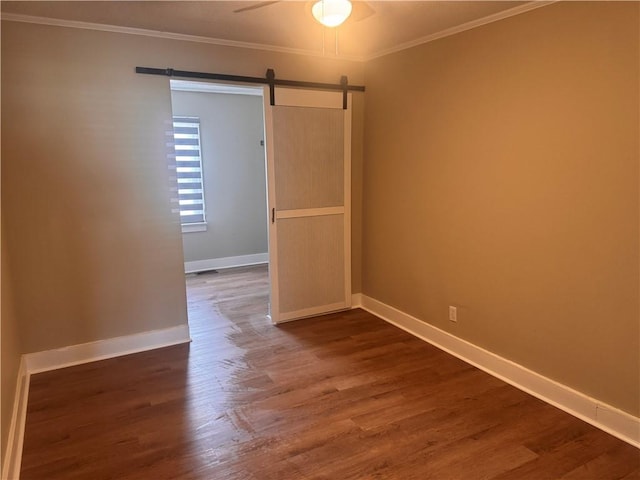 spare room featuring dark hardwood / wood-style floors, ceiling fan, ornamental molding, and a barn door