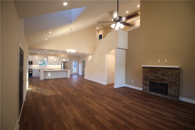 unfurnished living room featuring a fireplace, ceiling fan with notable chandelier, dark wood-type flooring, and a high ceiling