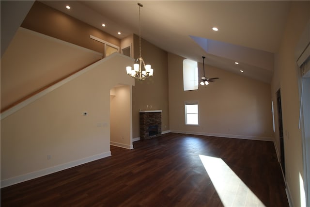 unfurnished living room with a fireplace, a towering ceiling, ceiling fan with notable chandelier, and dark wood-type flooring