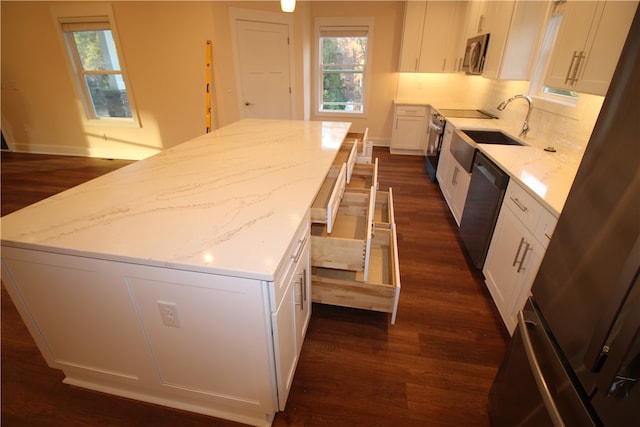 kitchen with appliances with stainless steel finishes, light stone counters, sink, a center island, and white cabinetry