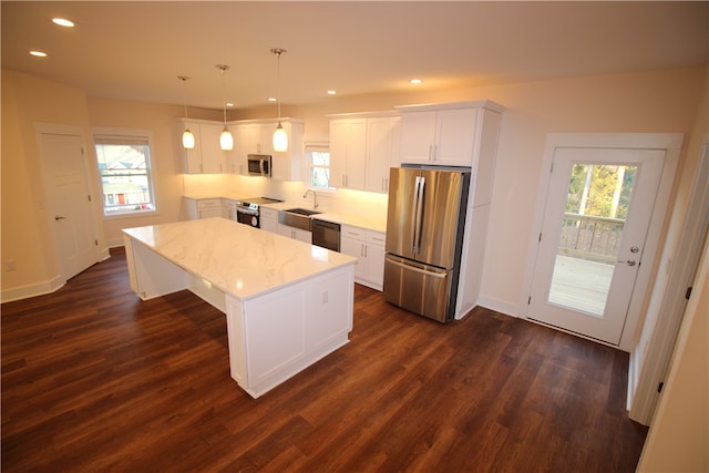 kitchen featuring stainless steel appliances, sink, pendant lighting, white cabinets, and a center island