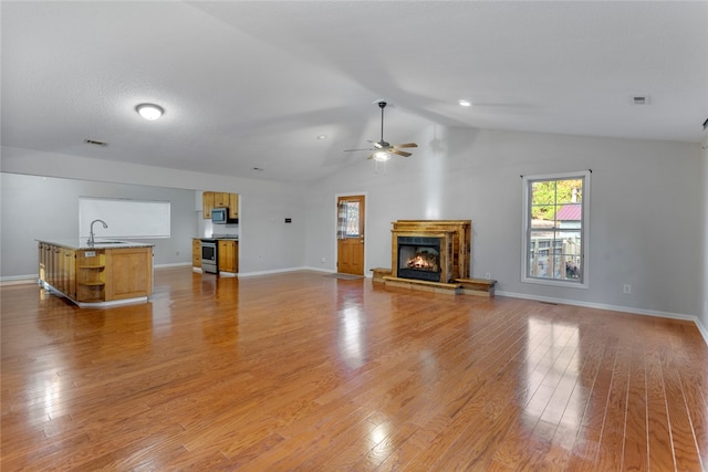 unfurnished living room featuring ceiling fan, light wood-type flooring, sink, and vaulted ceiling