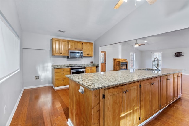 kitchen featuring sink, stainless steel appliances, light hardwood / wood-style flooring, vaulted ceiling, and a kitchen island with sink