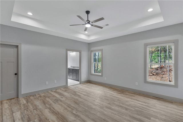 unfurnished bedroom featuring multiple windows, ensuite bathroom, ceiling fan, and light hardwood / wood-style floors