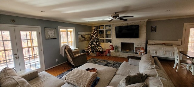 living room featuring french doors, ornamental molding, a large fireplace, ceiling fan, and light hardwood / wood-style floors