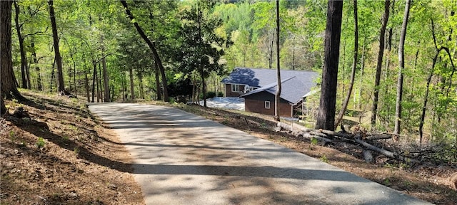 view of street featuring aphalt driveway and a wooded view