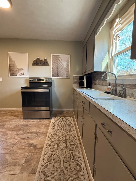 kitchen featuring backsplash, stainless steel electric stove, sink, gray cabinets, and decorative light fixtures