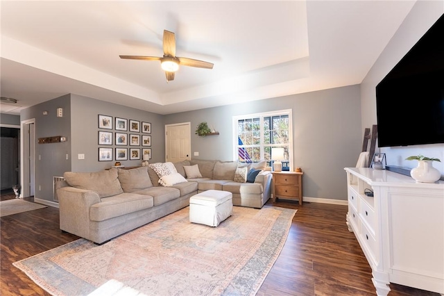 living room featuring dark wood-type flooring, ceiling fan, and a raised ceiling