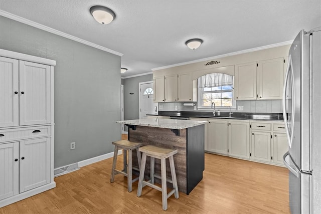 kitchen featuring stainless steel fridge, crown molding, light hardwood / wood-style floors, a kitchen bar, and a kitchen island