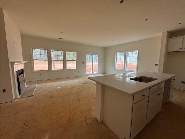 kitchen featuring a fireplace, a sink, white cabinetry, open floor plan, and a center island with sink