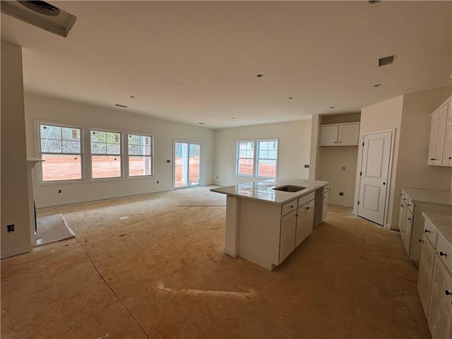 kitchen featuring light countertops, visible vents, open floor plan, a kitchen island with sink, and white cabinets