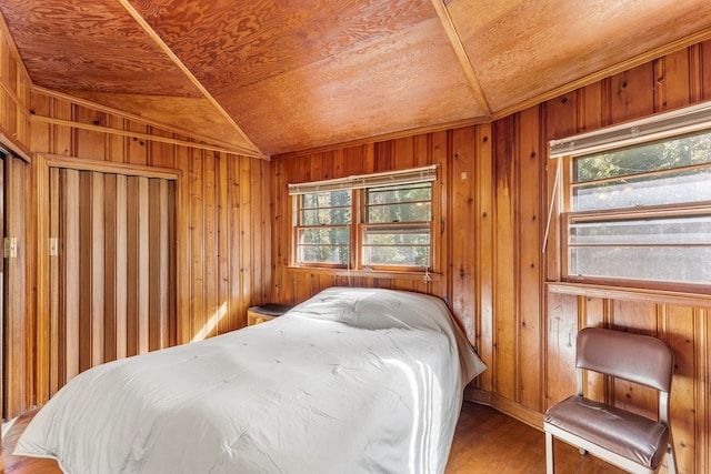 bedroom featuring multiple windows, wooden walls, wood-type flooring, and vaulted ceiling