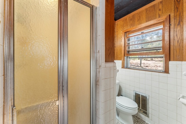 bathroom with wood walls, tile patterned floors, toilet, tile walls, and a shower with shower door