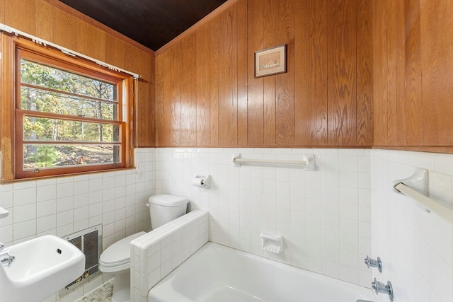 bathroom with a tub to relax in, toilet, tile walls, and wooden walls