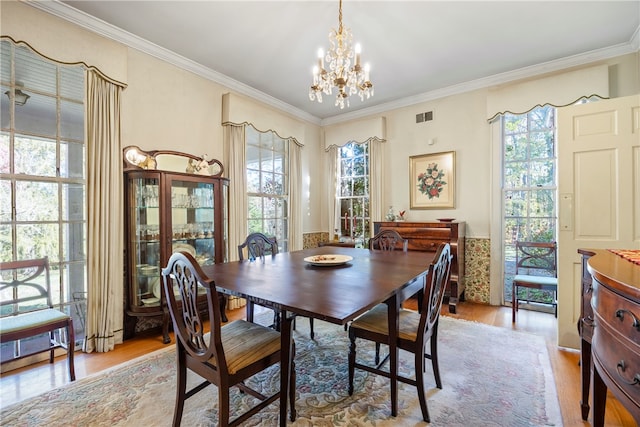 dining room featuring light wood-type flooring, ornamental molding, and an inviting chandelier