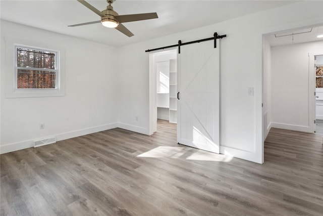 empty room featuring hardwood / wood-style floors, a barn door, and ceiling fan