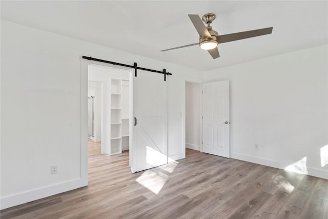 unfurnished bedroom with ceiling fan, a barn door, a spacious closet, light hardwood / wood-style flooring, and a closet