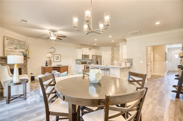 dining space with a stone fireplace, ornamental molding, and light hardwood / wood-style floors