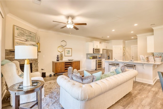 living room featuring ceiling fan, ornamental molding, a fireplace, and light hardwood / wood-style floors