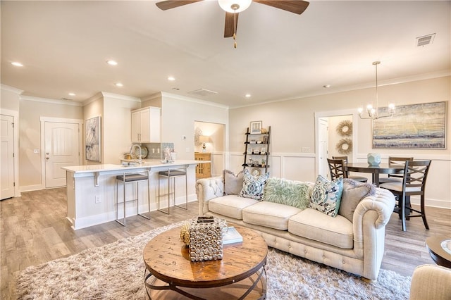 living room with crown molding, sink, ceiling fan with notable chandelier, and light wood-type flooring