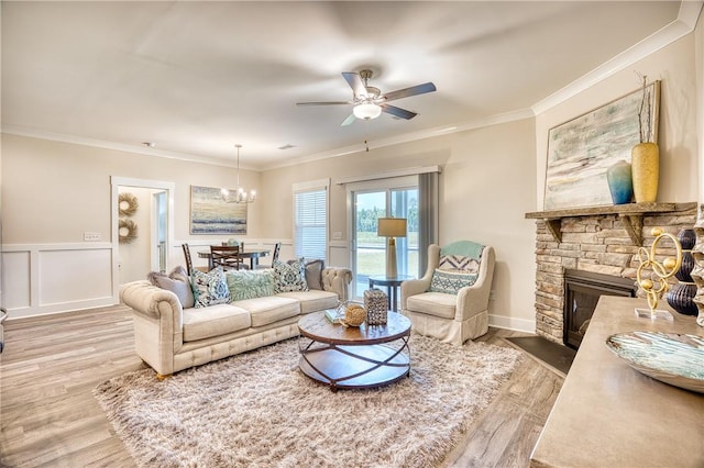 living room with crown molding, wood-type flooring, a fireplace, and ceiling fan with notable chandelier