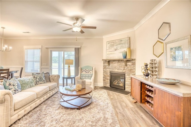 living room with ornamental molding, ceiling fan with notable chandelier, a fireplace, and light hardwood / wood-style flooring