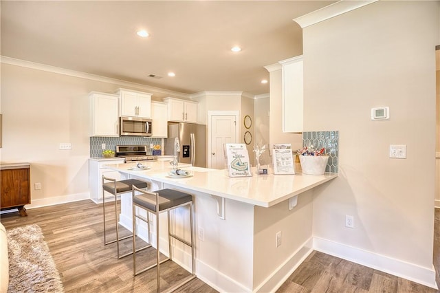 kitchen with a breakfast bar area, kitchen peninsula, white cabinets, and appliances with stainless steel finishes