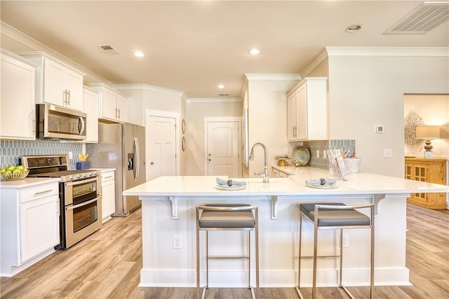 kitchen featuring a breakfast bar, white cabinets, light hardwood / wood-style floors, kitchen peninsula, and stainless steel appliances