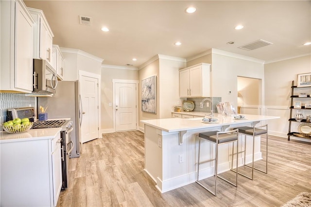 kitchen with white cabinetry, a breakfast bar area, kitchen peninsula, stainless steel appliances, and light hardwood / wood-style flooring