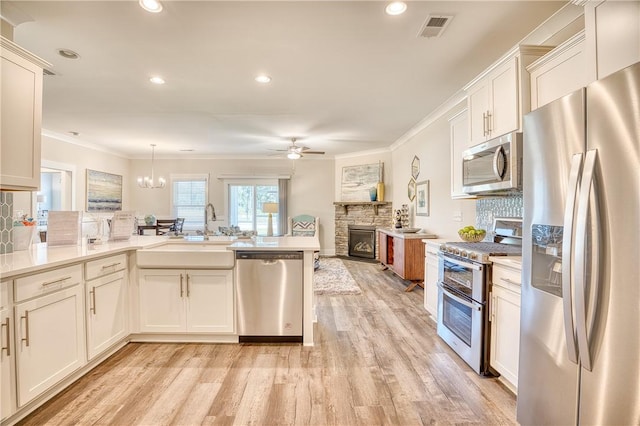 kitchen featuring sink, appliances with stainless steel finishes, hanging light fixtures, a fireplace, and ornamental molding