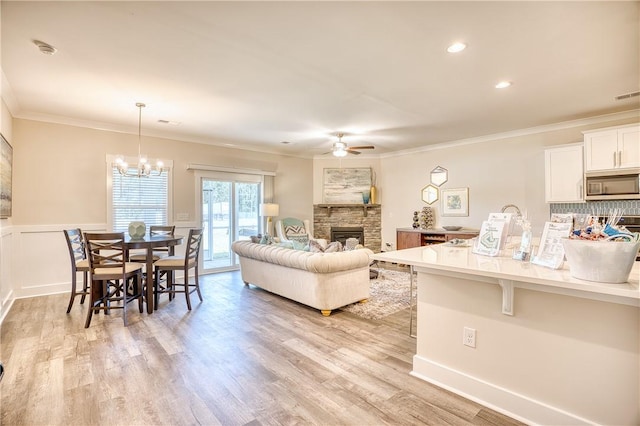 living room featuring light hardwood / wood-style flooring, ceiling fan with notable chandelier, a fireplace, and ornamental molding