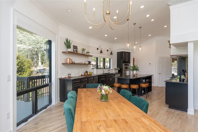 dining area featuring crown molding, sink, an inviting chandelier, and light wood-type flooring