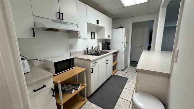 kitchen featuring sink, light tile patterned floors, white fridge, a paneled ceiling, and white cabinets