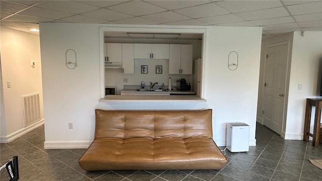 interior space featuring a paneled ceiling, white cabinetry, dark tile patterned floors, and sink