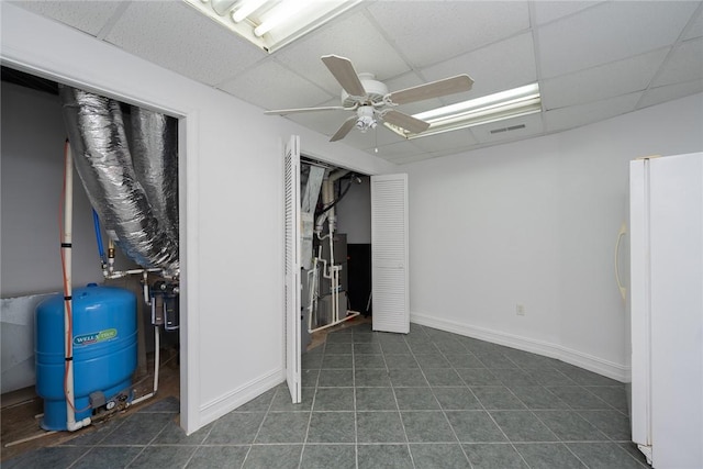 basement featuring dark tile patterned flooring, ceiling fan, white refrigerator, and a drop ceiling