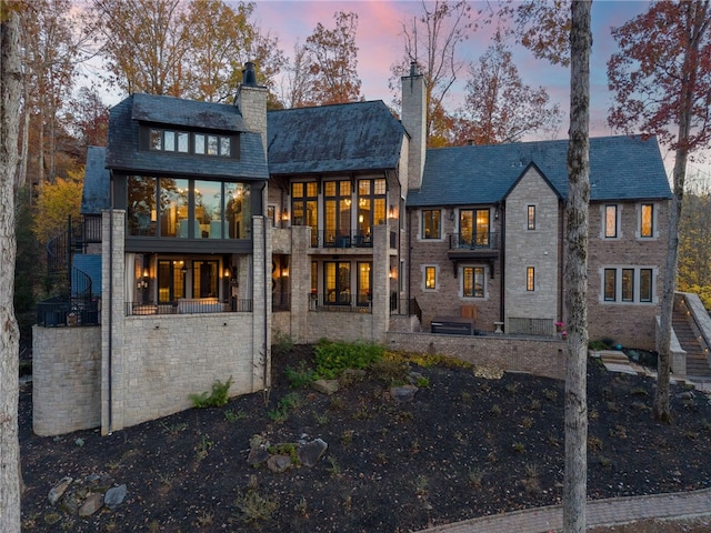 rear view of property with stone siding, a chimney, a high end roof, and a balcony