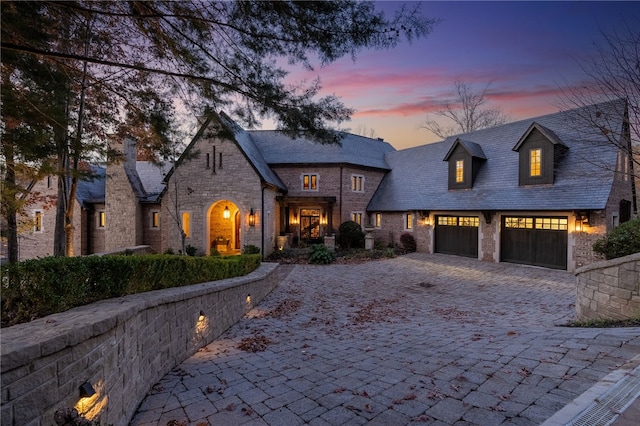 view of front of home with stone siding, decorative driveway, and a high end roof