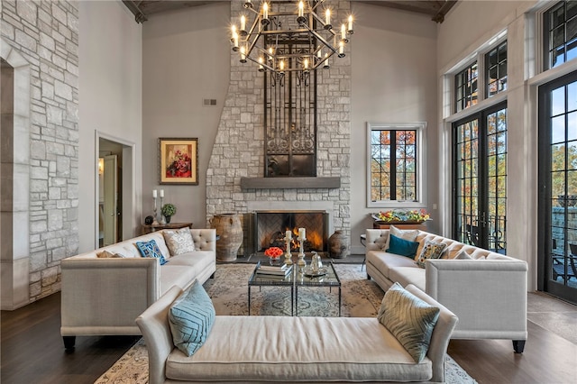 living area featuring a towering ceiling, french doors, wood finished floors, and a stone fireplace