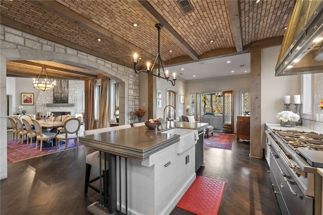 kitchen with white cabinetry, sink, decorative light fixtures, a fireplace, and a center island with sink