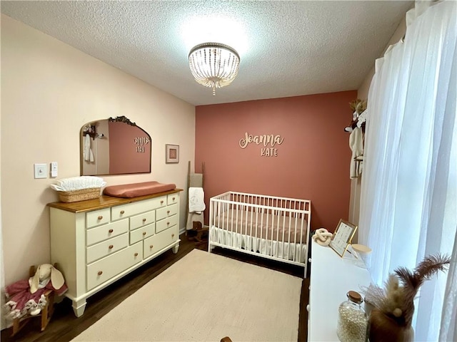 bedroom featuring a crib, a textured ceiling, dark hardwood / wood-style floors, and a notable chandelier