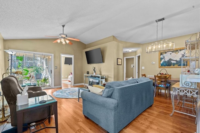 living room featuring a textured ceiling, hardwood / wood-style floors, ceiling fan with notable chandelier, and lofted ceiling