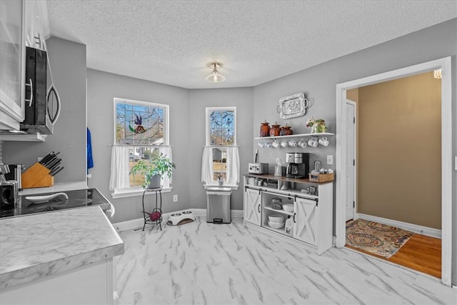 kitchen with a textured ceiling, light hardwood / wood-style flooring, white cabinetry, and black range oven