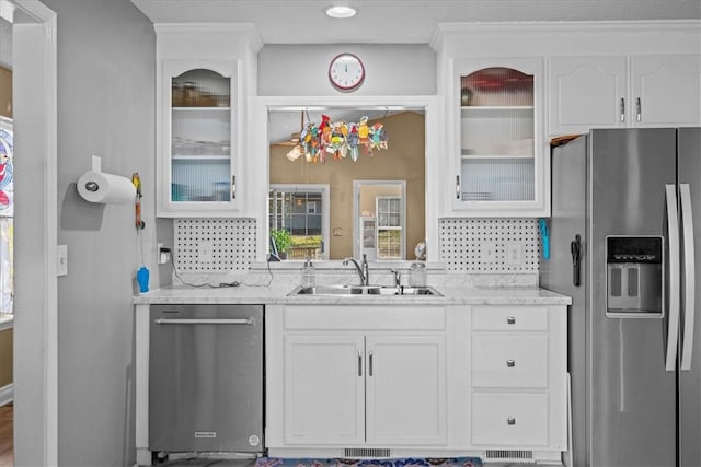 kitchen with backsplash, light stone counters, stainless steel appliances, sink, and white cabinets