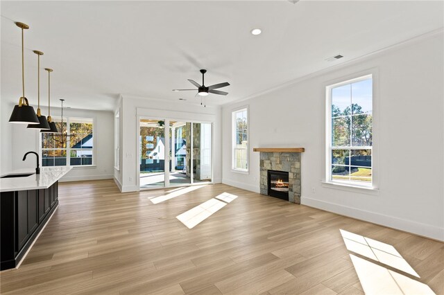 unfurnished living room with a stone fireplace, light hardwood / wood-style flooring, and a healthy amount of sunlight