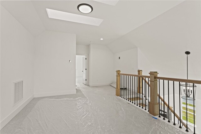hallway featuring vaulted ceiling with skylight and light colored carpet
